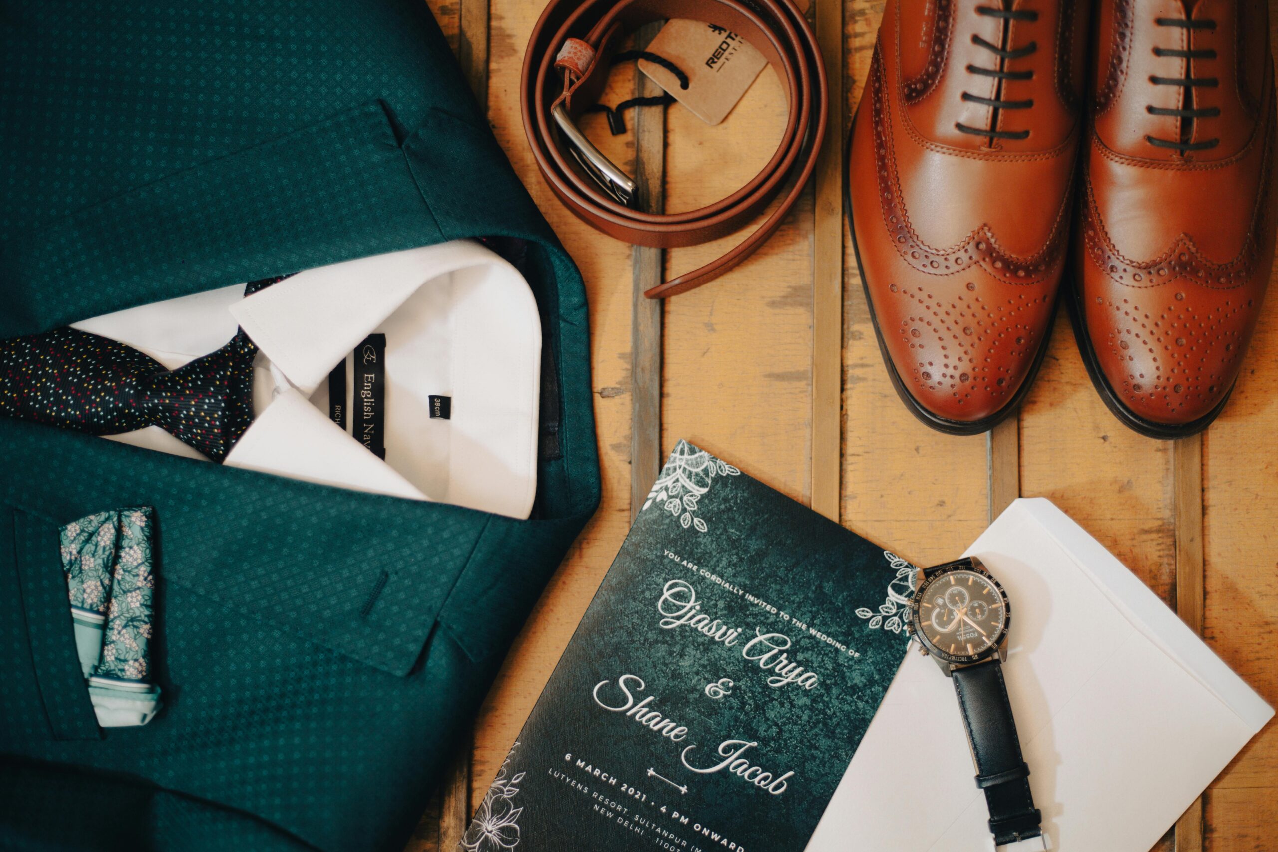 Classic men's wedding accessories flat lay featuring suit, shoes, and invitation.