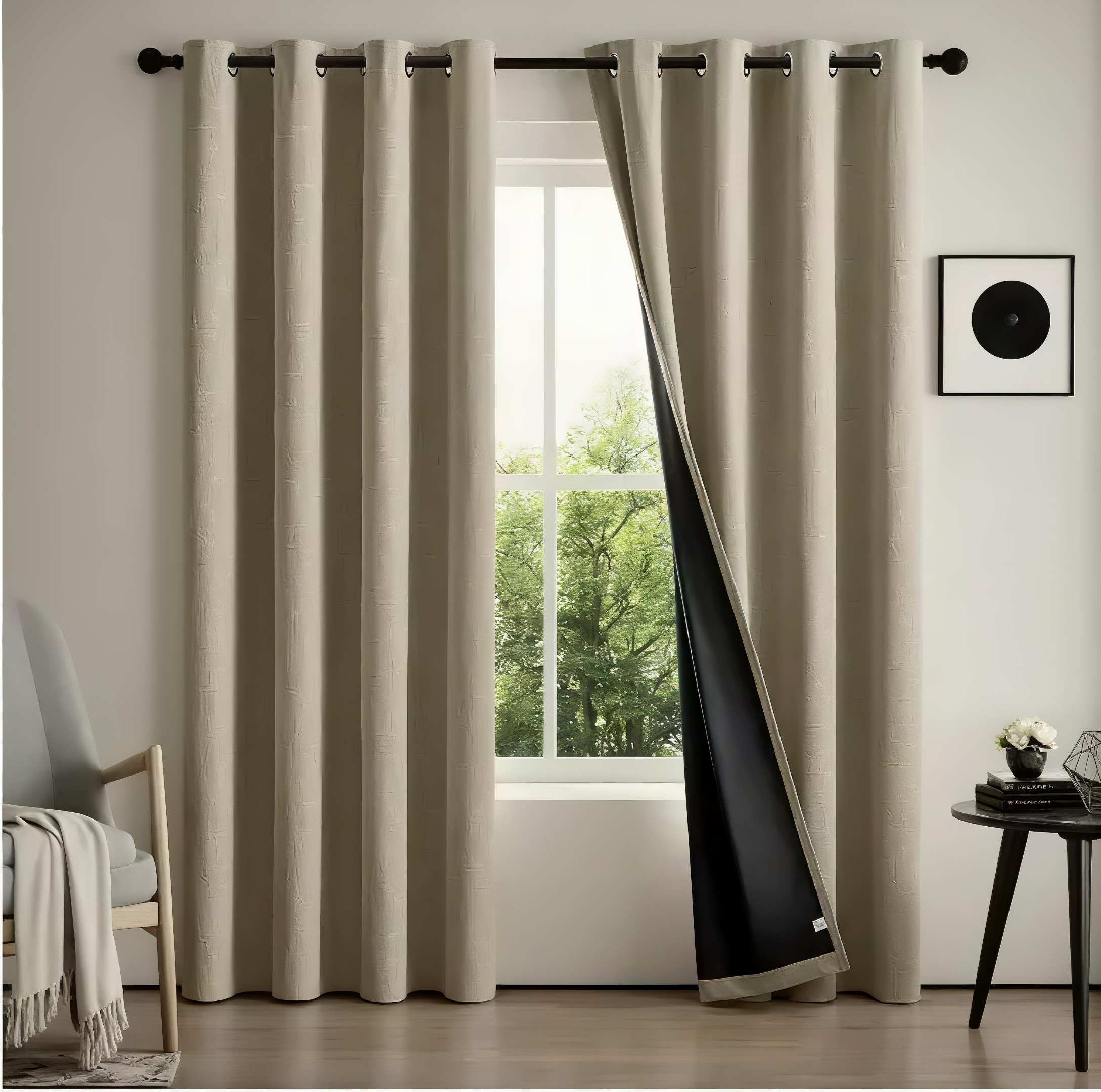 Beige blackout curtains hanging from a black rod over a window, with one panel pulled back to reveal a dark lining and an outdoor view of green trees.