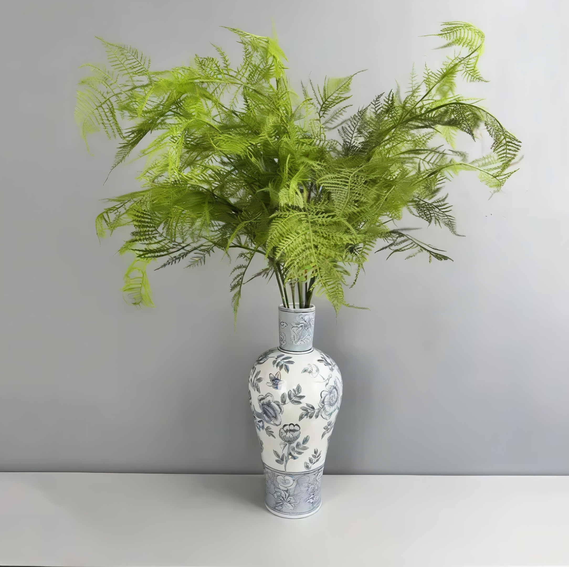A tall, slender white porcelain vase decorated with blue floral patterns holding a wild, sprawling arrangement of bright green faux fern branches.