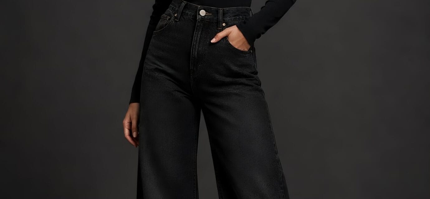 A studio portrait of a woman wearing ink black wide leg jeans and a matching black turtleneck sweater.