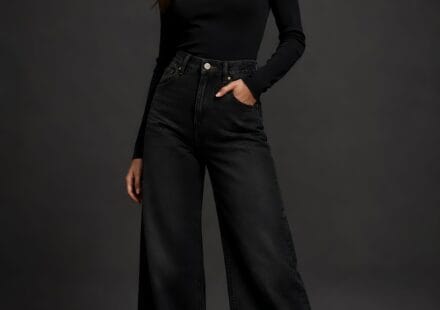 A studio portrait of a woman wearing ink black wide leg jeans and a matching black turtleneck sweater.